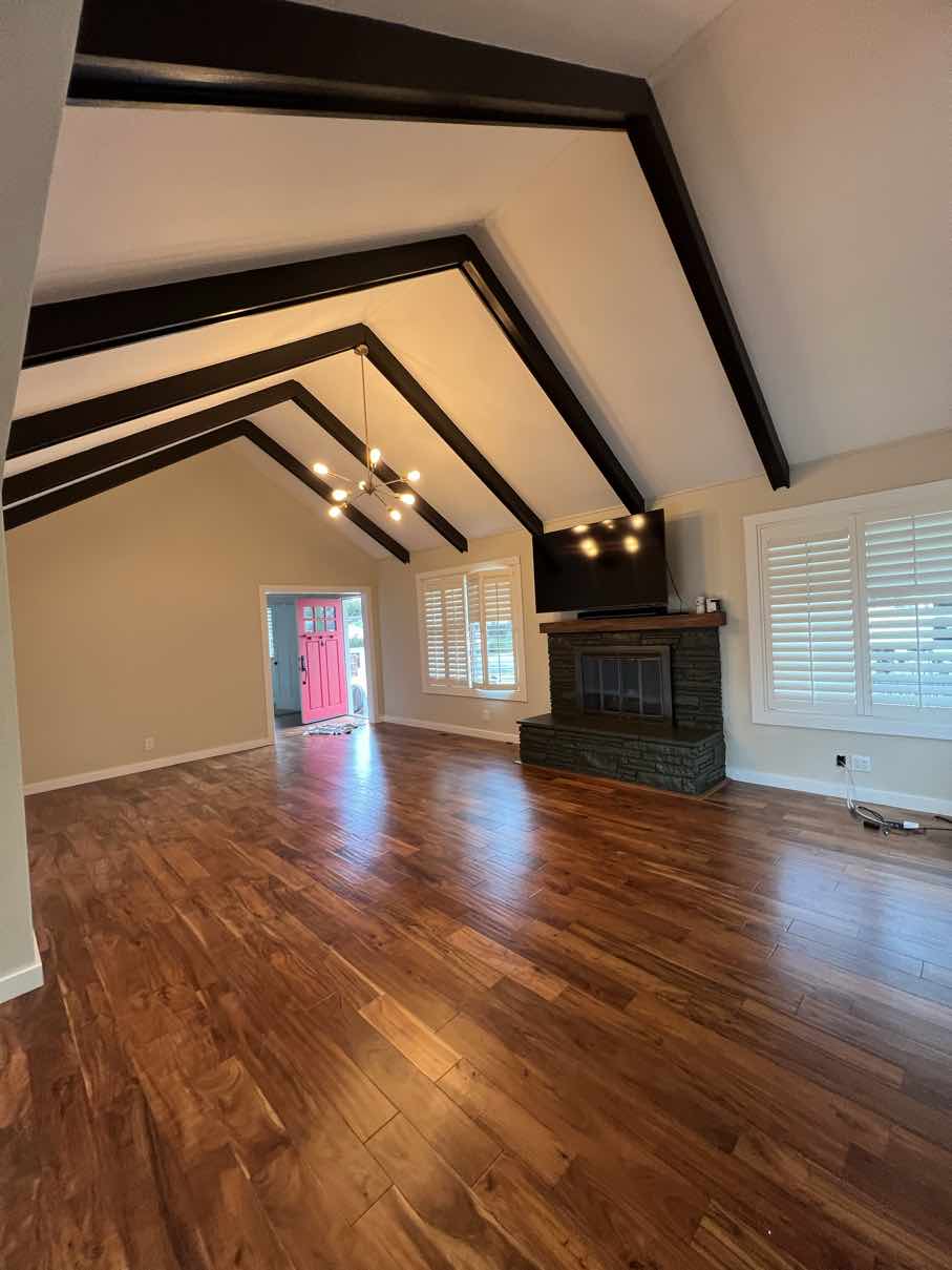 Vaulted living room transformed with fresh paint, a dark stacked-stone fireplace surround, and warm wood floors